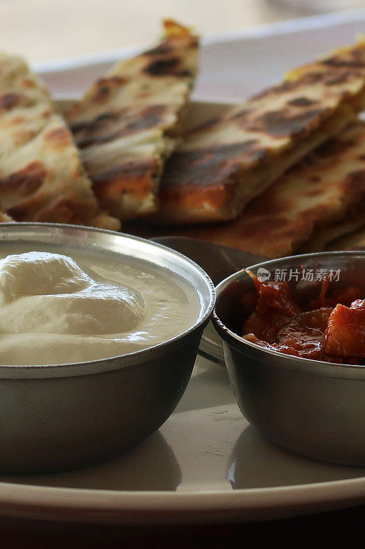 这是印度自助早餐的特写，白色的盘子上放着三角形的aloo paratha切片，上面撒着焦糖洋葱，美味的面包里塞满了garam masala土豆，酒店餐厅aloo paratha菜，raita凝乳酸奶